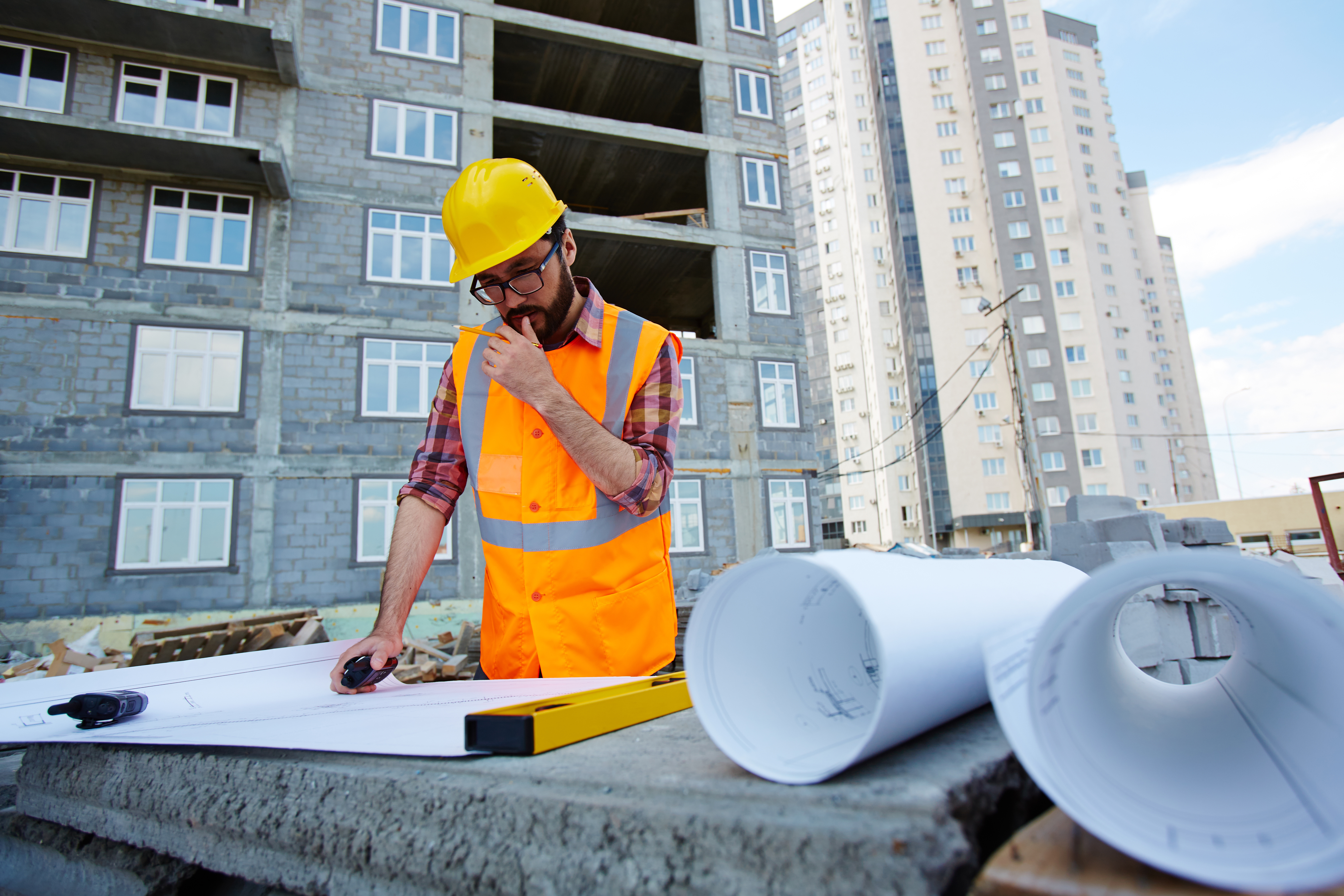 Pensive worker in hardhat and uniform looking at sketch of new building